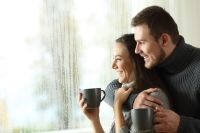 Happy couple holding mugs and looking out the window